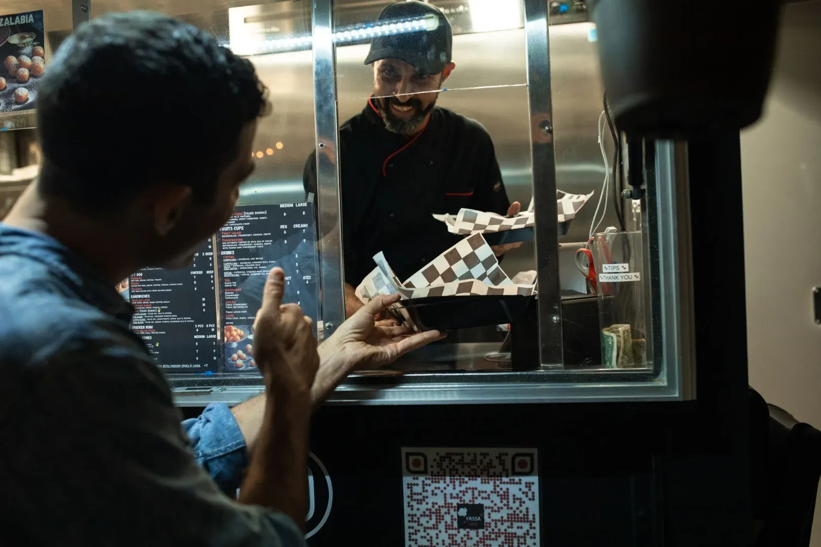 A man is ordering food from a chef inside a street food truck at night.