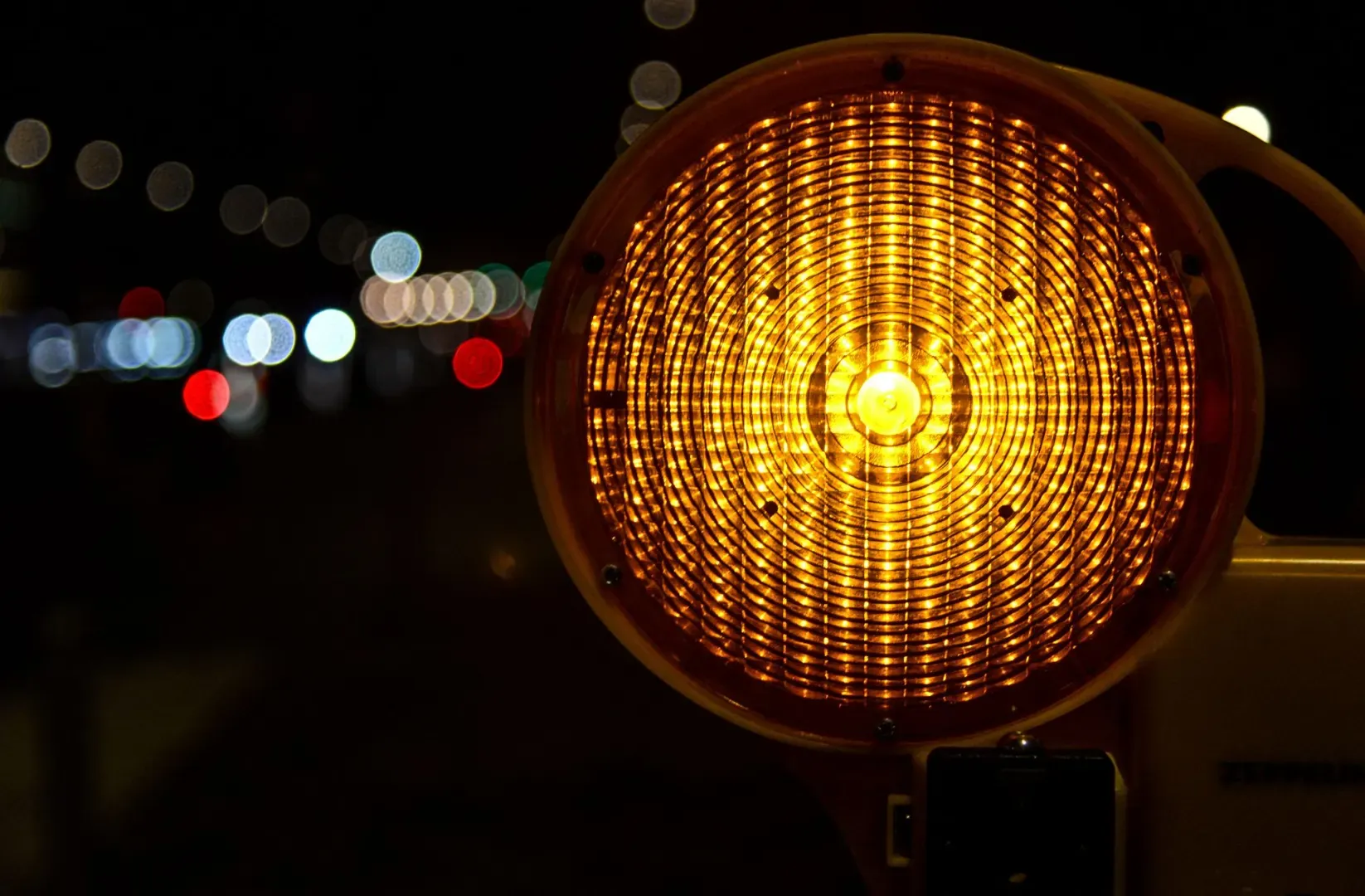 A reflective traffic warning light glowing in the nighttime with bokeh effect.