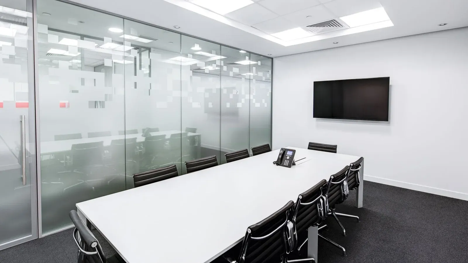 Sleek, minimalist conference room with glass walls, long table, and office chairs.