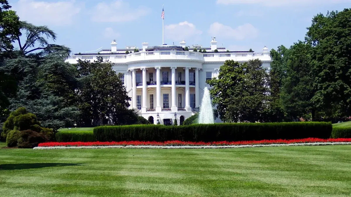 Iconic view of the White House with lush gardens and a central fountain on a sunny day.