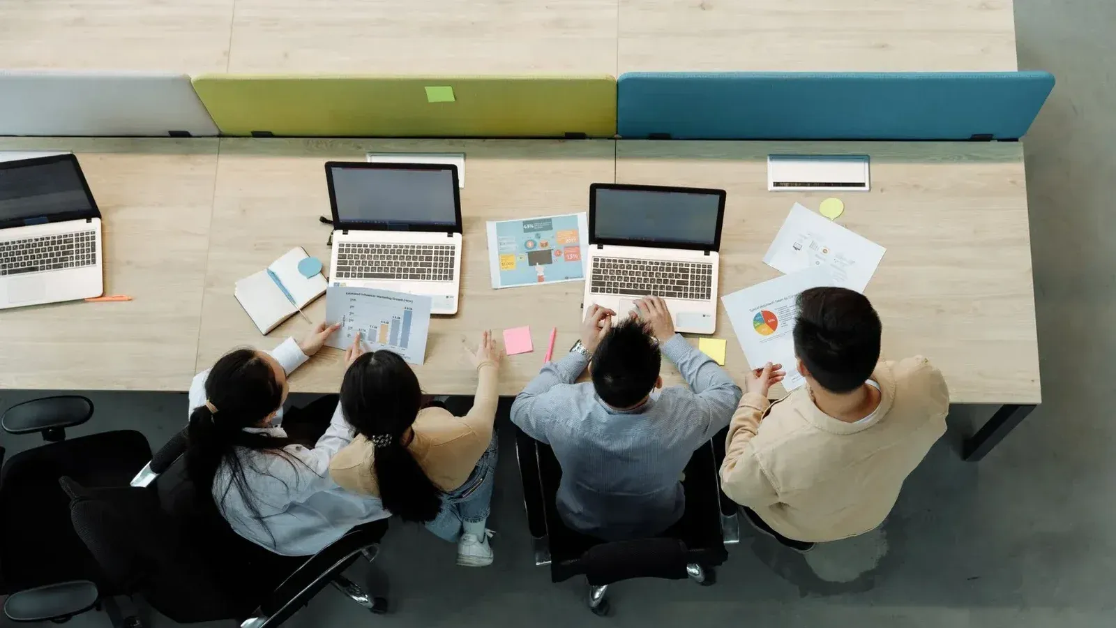 Aerial view of four colleagues working with laptops and documents at a shared desk.