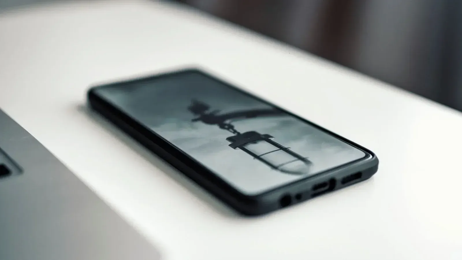 Close-up de un smartphone que muestra una imagen borrosa, colocada en un escritorio junto a una computadora portátil.