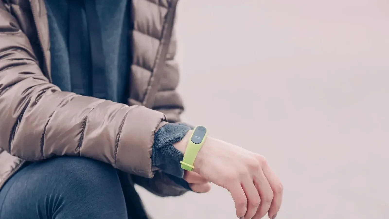 A person wearing a green fitness tracker and winter clothing outdoors. Perfect for health and lifestyle themes.