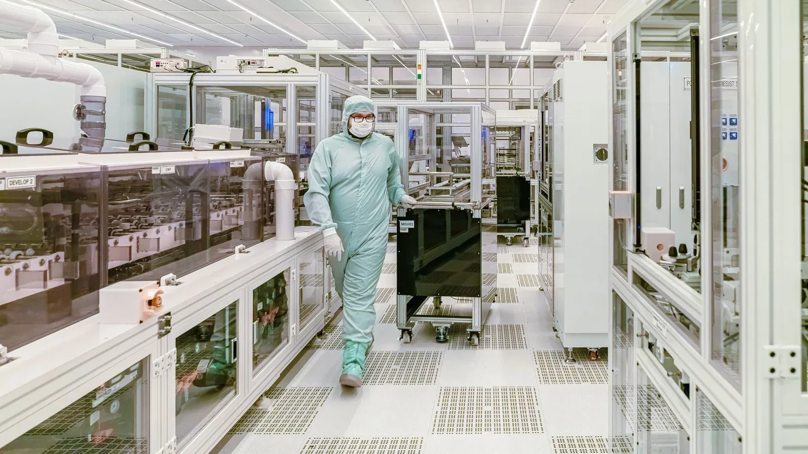 Scientist in protective gear walking in a high-tech cleanroom laboratory environment.