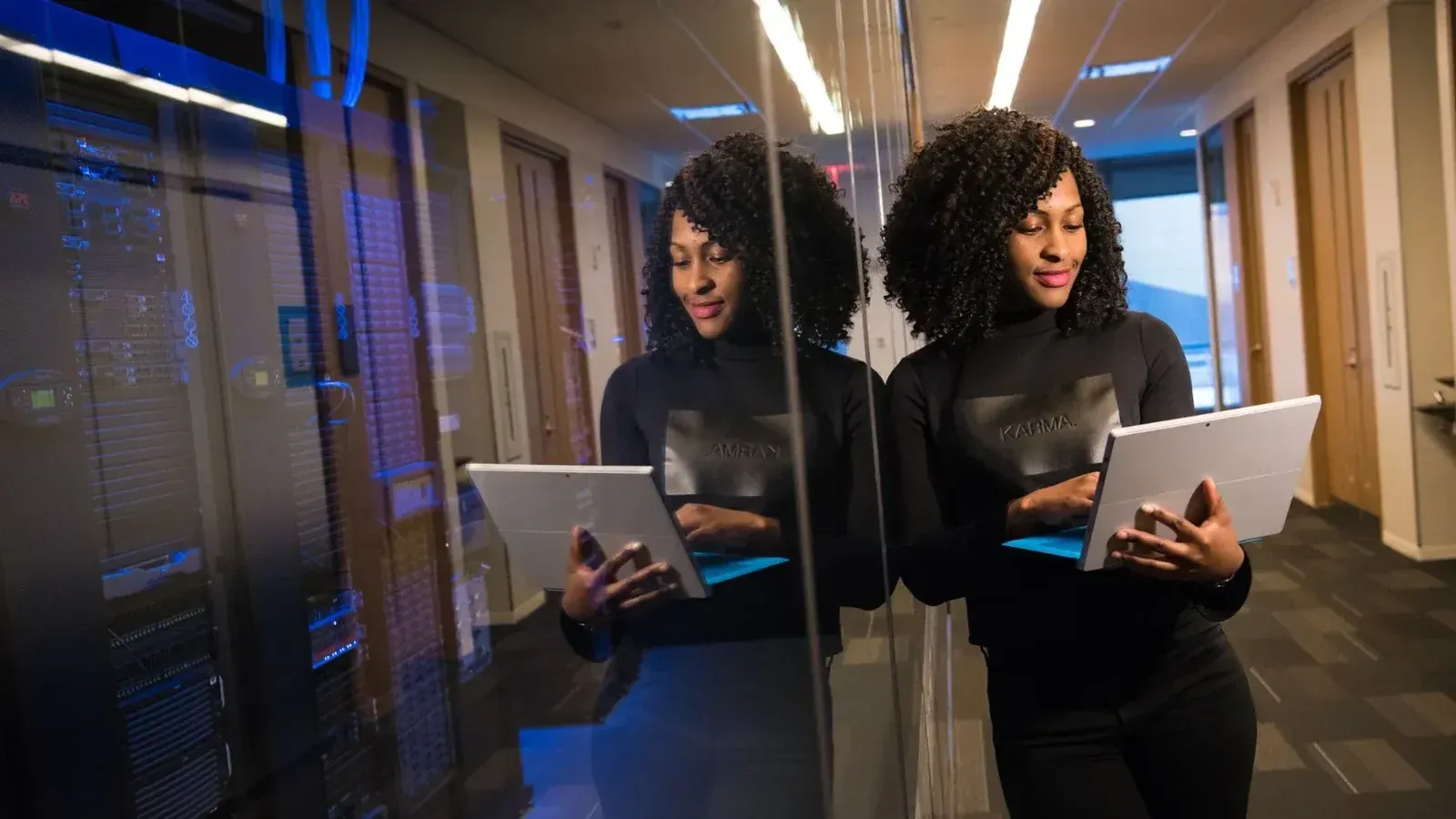 African American woman standing in modern office using laptop, reflecting professionalism and technology engagement.