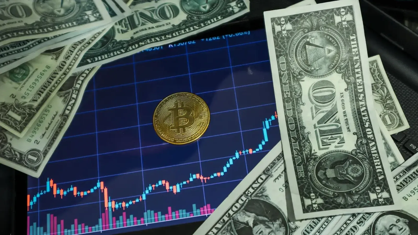 Bitcoin coin on a tablet showing stock chart, surrounded by dollar bills.