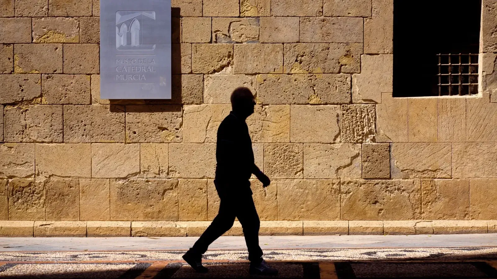 Silhouette of a man walking by Museo de la Catedral wall in Murcia, Spain.