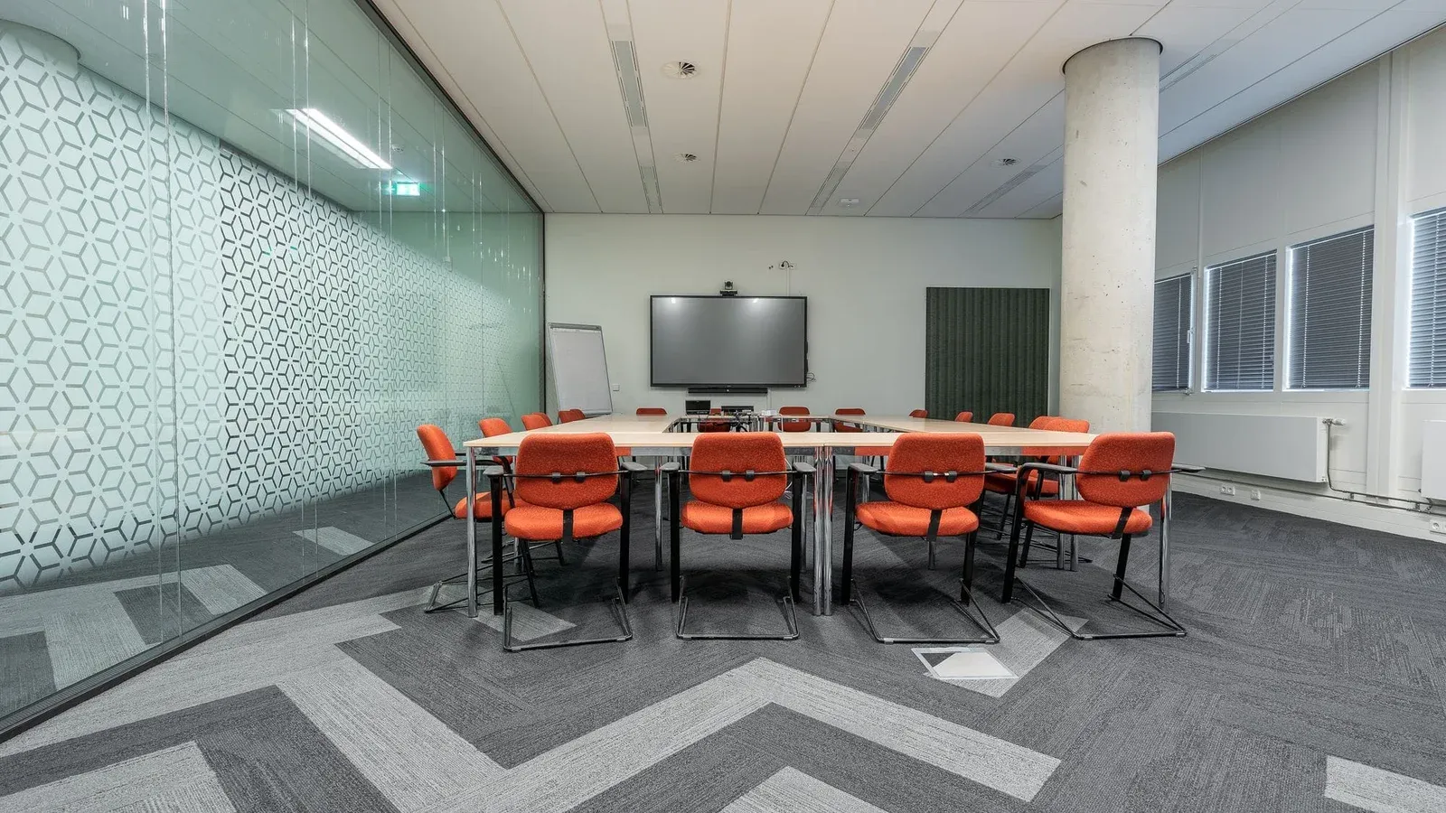 Spacious conference room with a large meeting table, red chairs, and glass walls for natural lighting.