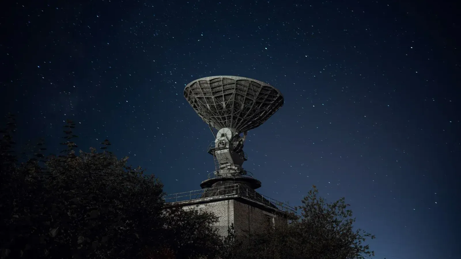 Radio telescope and green lush trees under blue sky with stars at night