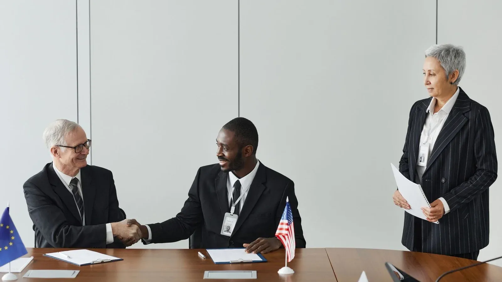 Multinational business meeting with agreement signing, featuring diverse professionals and flags.