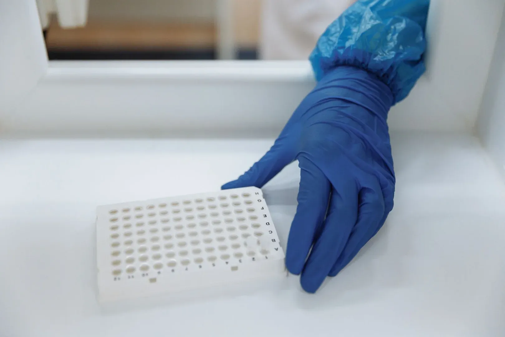 Científico con guantes de protección manipulando muestras de prueba en un entorno de laboratorio estéril.