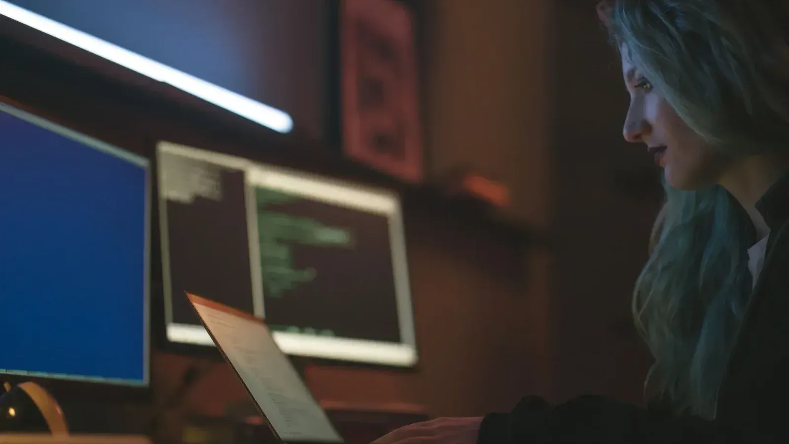 Mujer trabajando en programación de ciberseguridad con ordenadores portátiles y múltiples pantallas