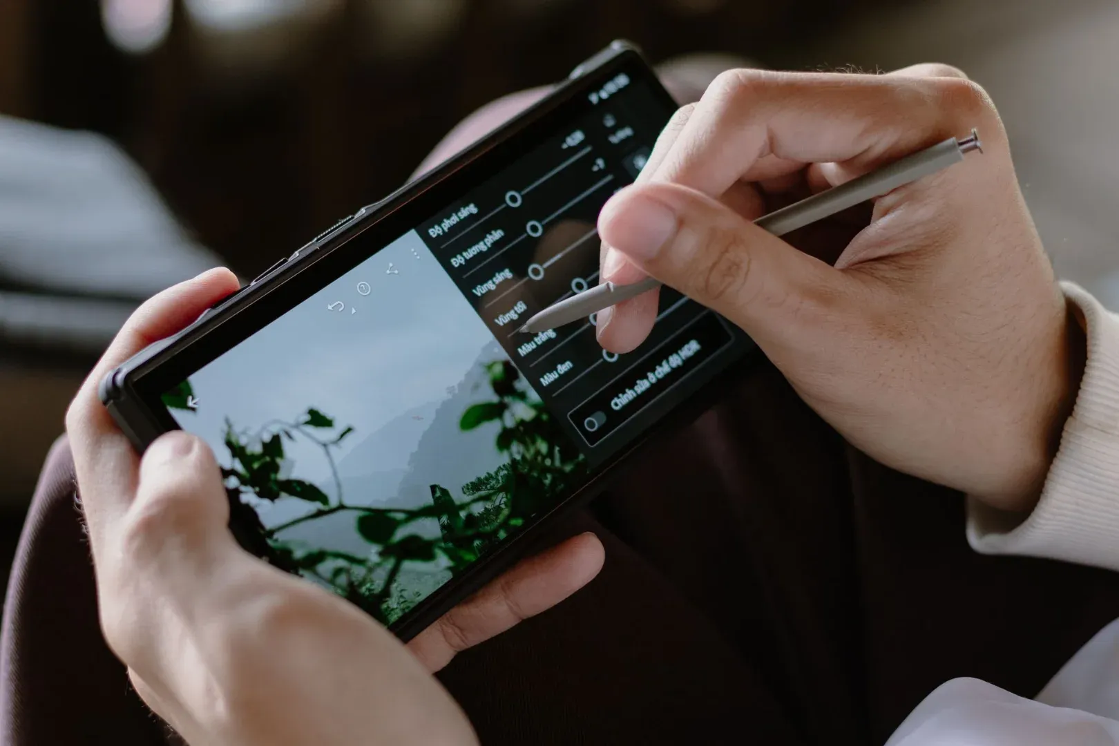 Close-up of a person editing photos on a smartphone with a stylus indoors.