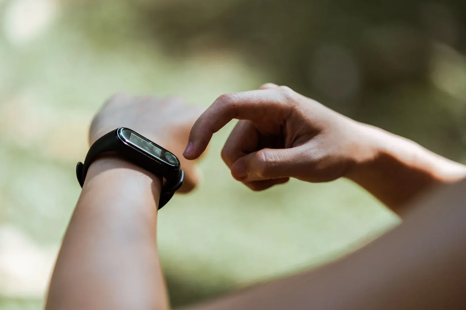 Crop anonymous person tapping modern wearable device with rectangular display while using gadget on blurred background in daylight