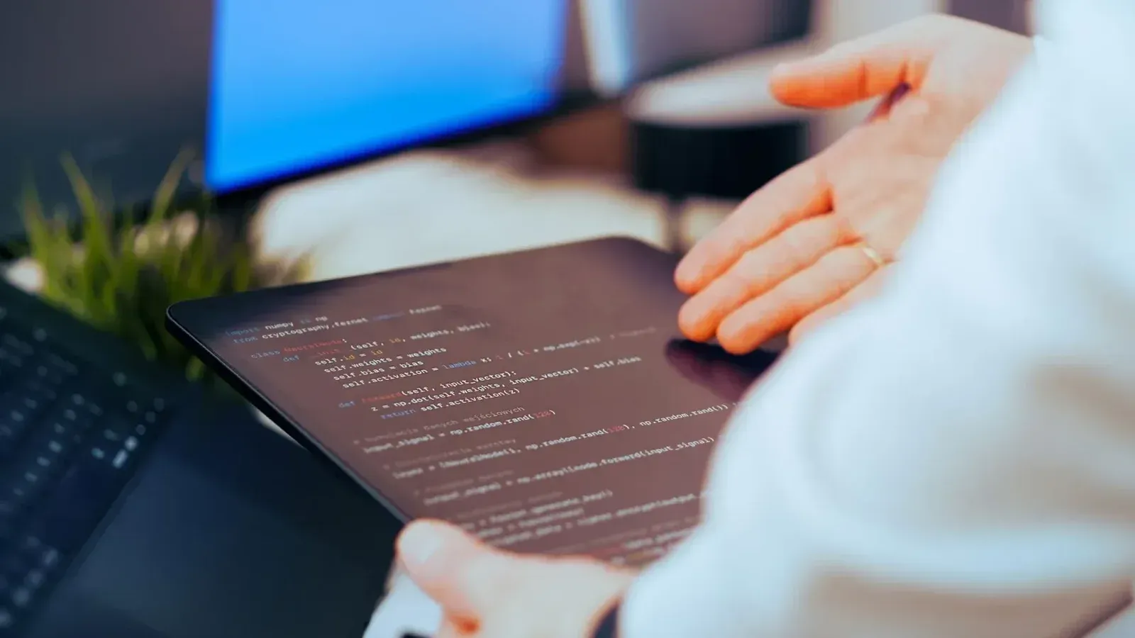 Software developer analyzing code on a tablet in a modern office workspace.