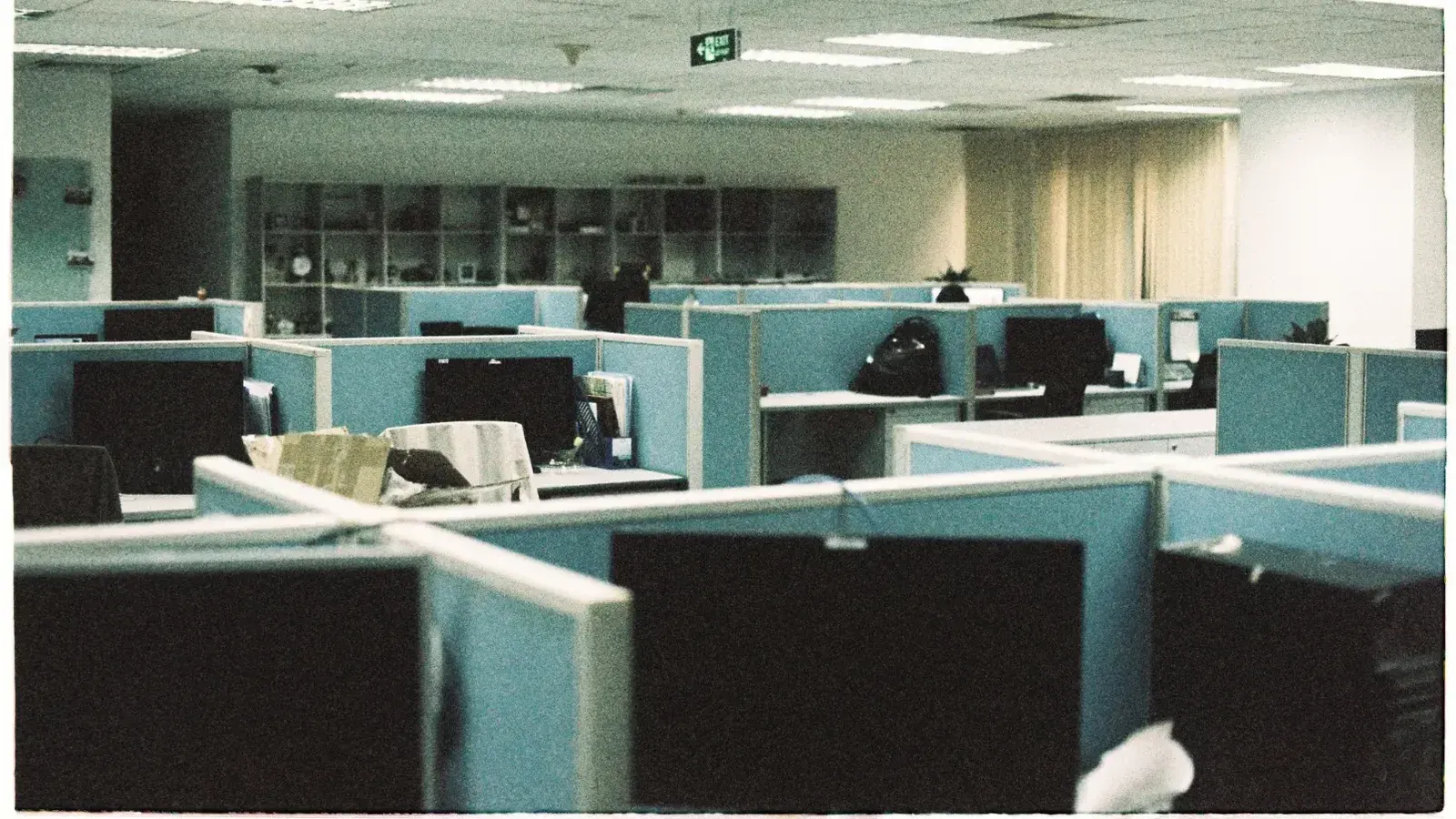 Amplio piso de oficina con filas de cubículos vacíos y monitores de computadora.