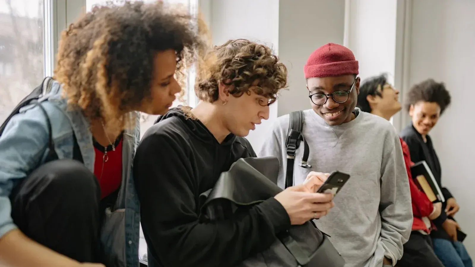 A group of diverse college students hanging out indoors and using a smartphone together.