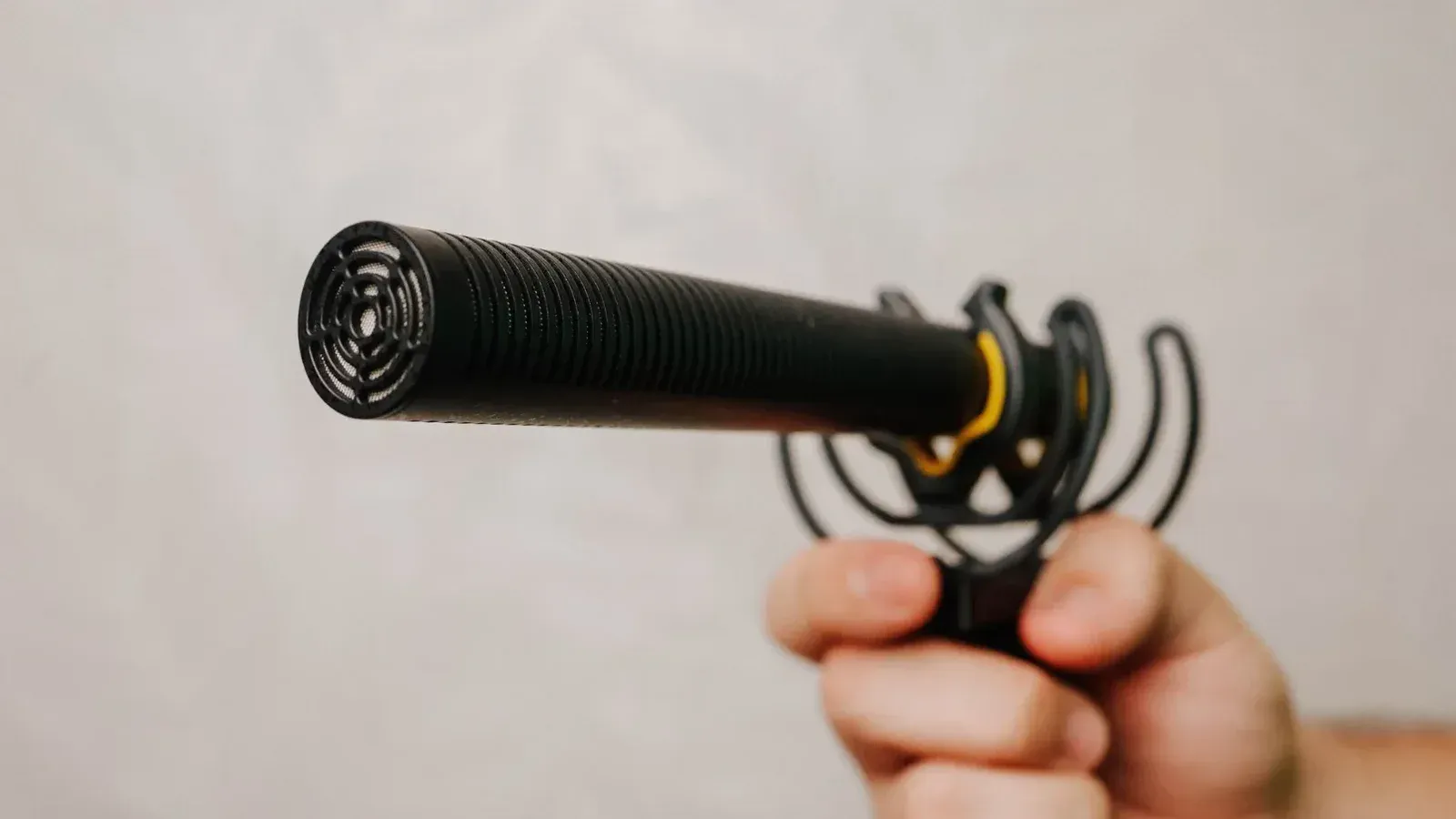 Mano sosteniendo un micrófono de escopeta con cubierta de espuma, ideal para grabación de voz y captura de audio.