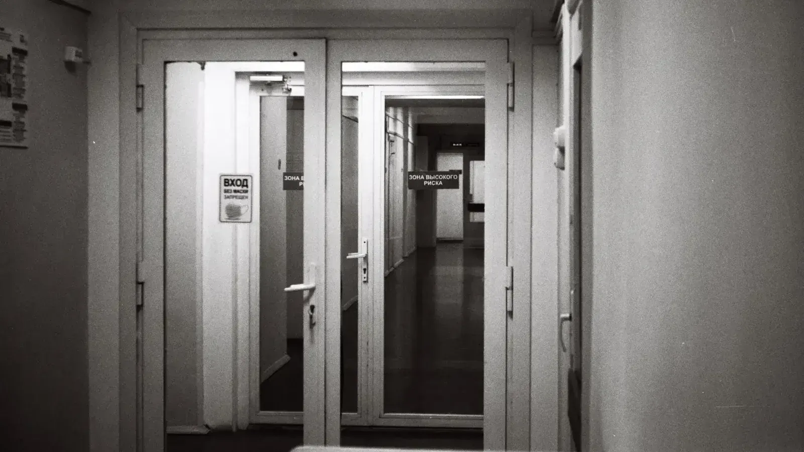 Empty hospital corridor in black and white, emphasizing open doors and healthcare environment.