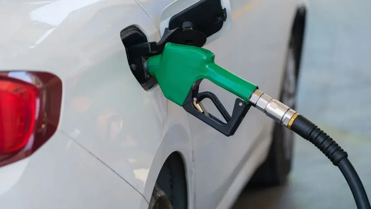 Close-up de una boquilla verde repostando un coche blanco en una gasolinera.