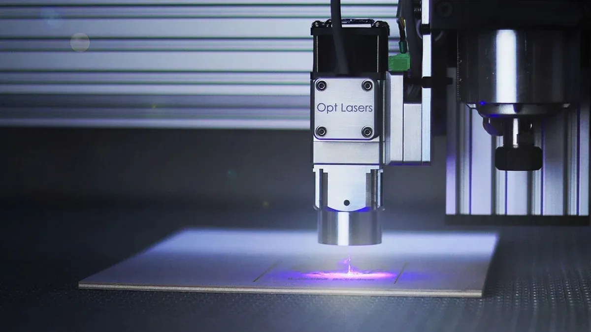 Close-up of a laser engraver working on a surface under blue lighting.