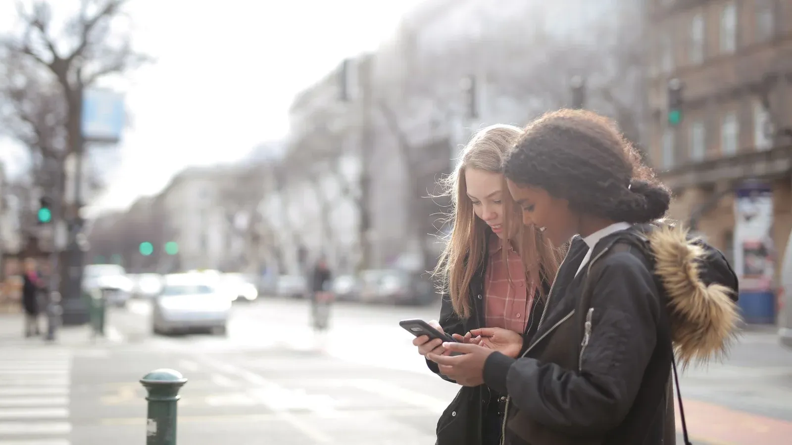 Two young women looking at a smartphone on a bustling urban street during the day.