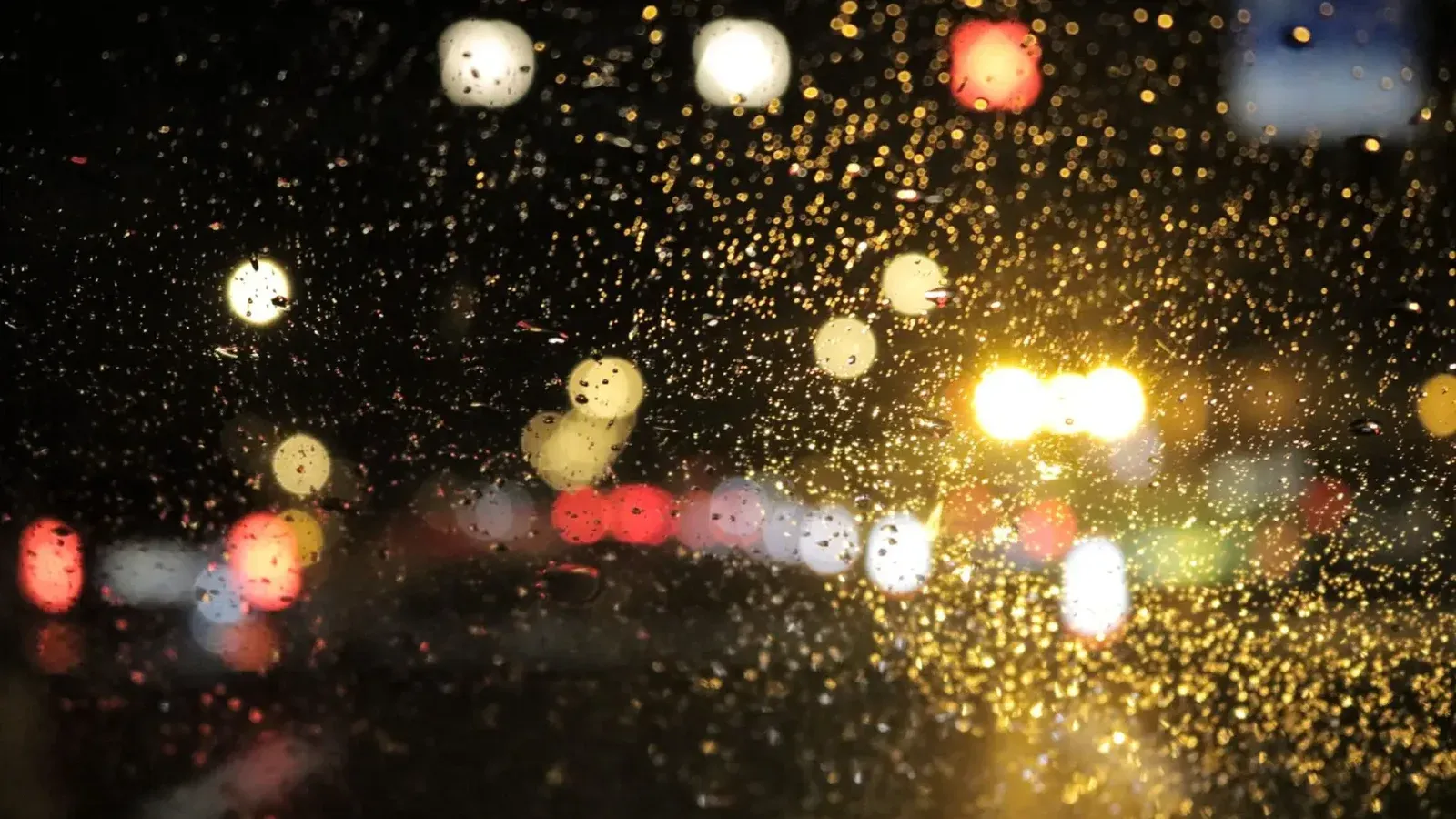 Street lights glistening through raindrops on a car window at night, creating a bright bokeh effect.