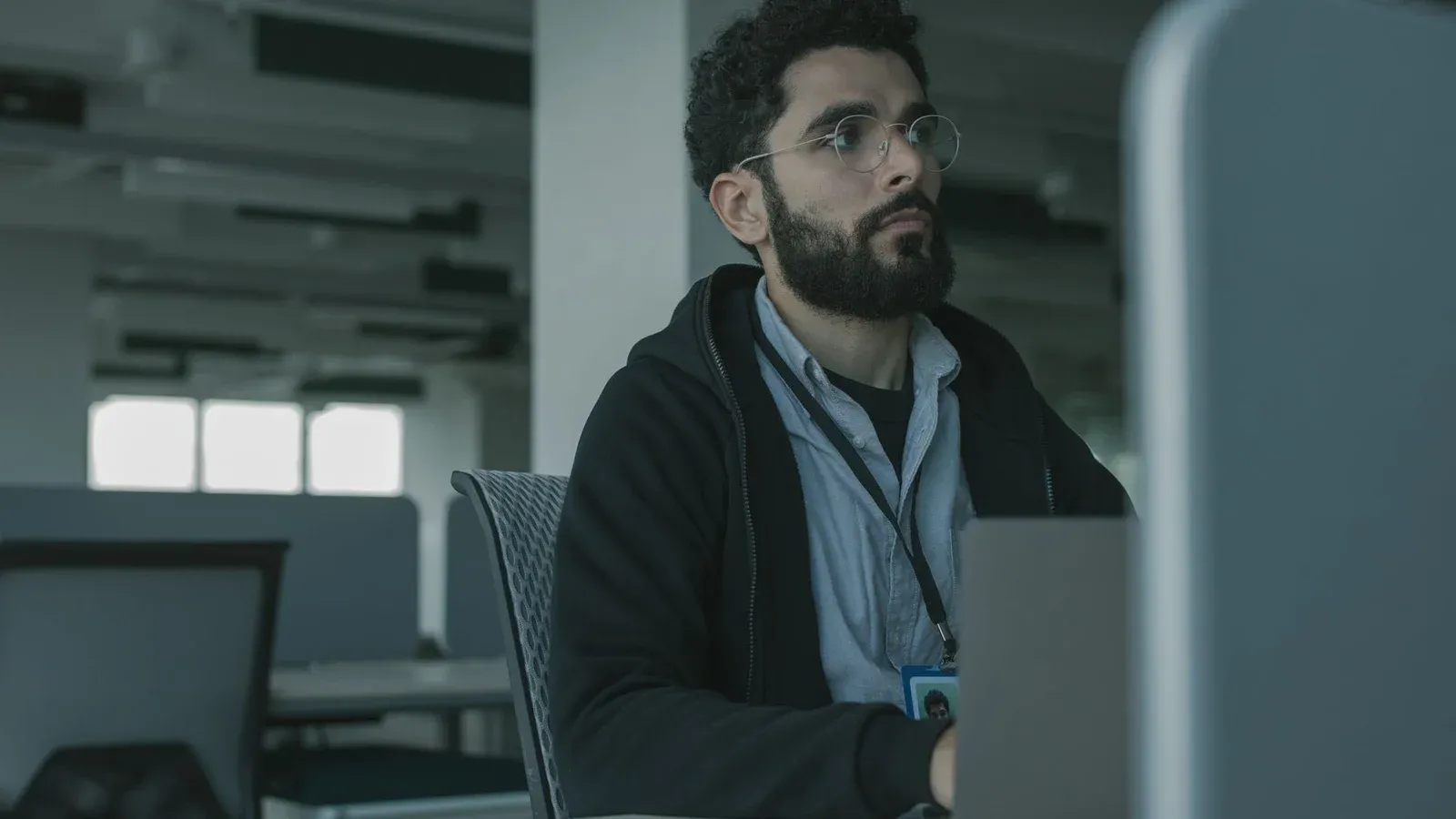 Man with eyeglasses working at a desk in an office setting, focused and engaged.