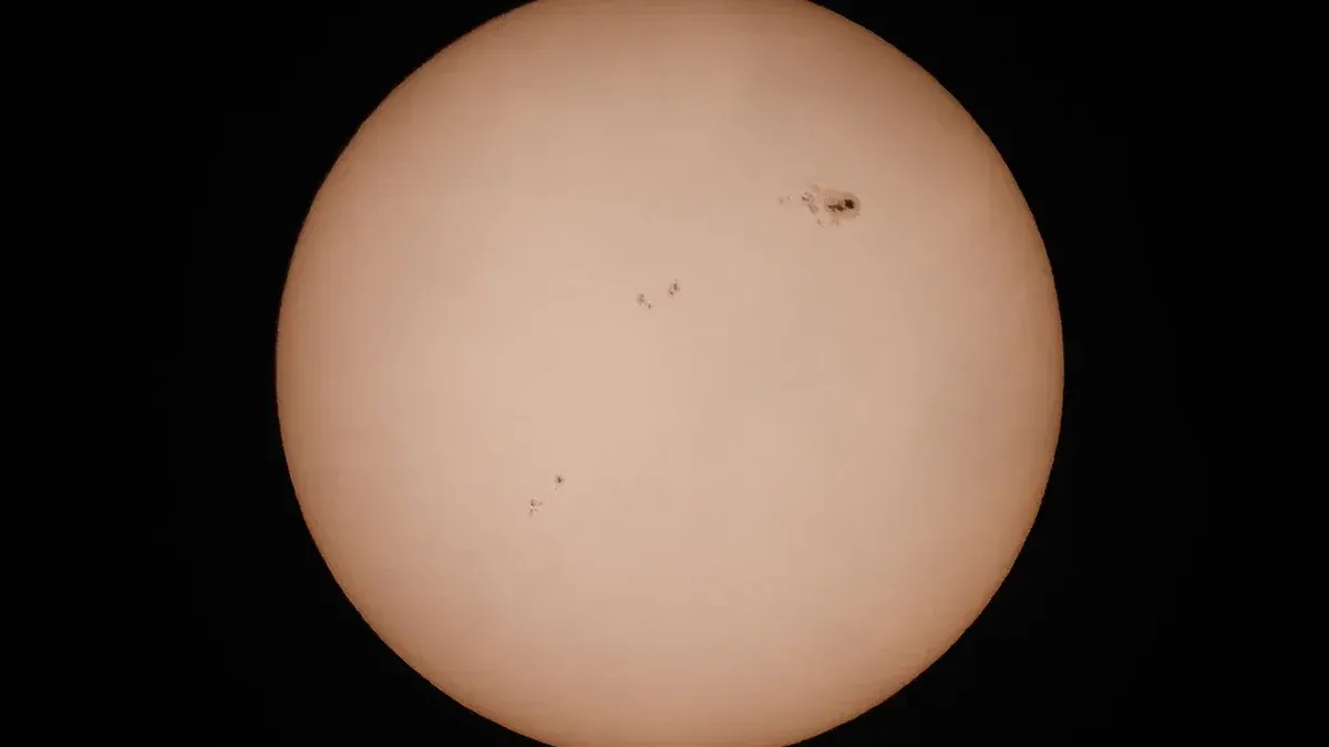 A detailed photograph of the sun highlighting visible sunspots against a dark background.