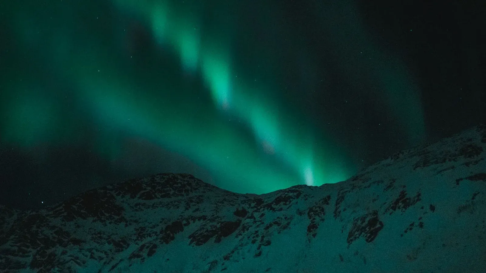 Majestic aurora borealis illuminates the night sky over snow-covered mountains.