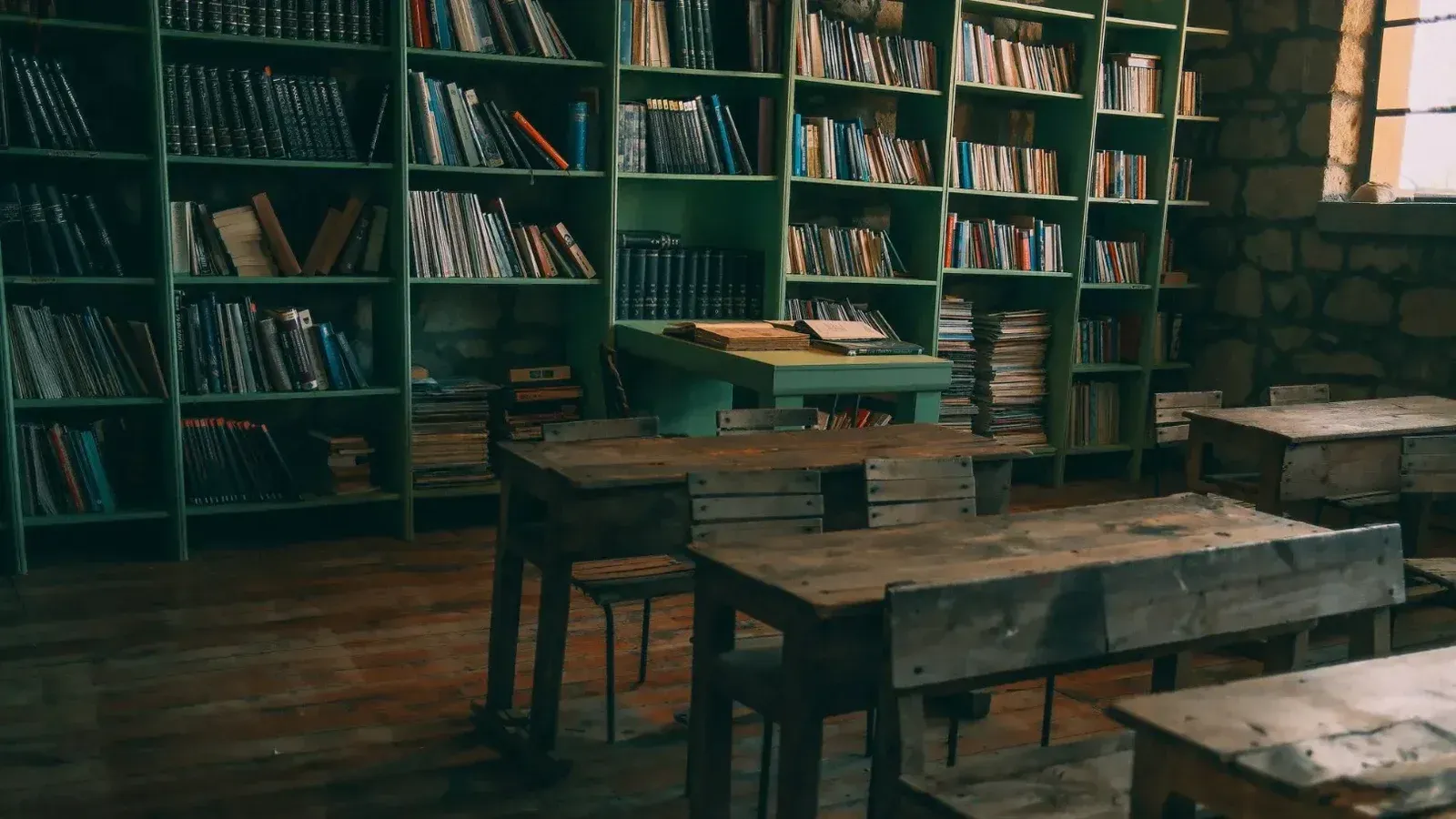 A rustic, vintage classroom featuring wooden desks and bookshelves filled with books.