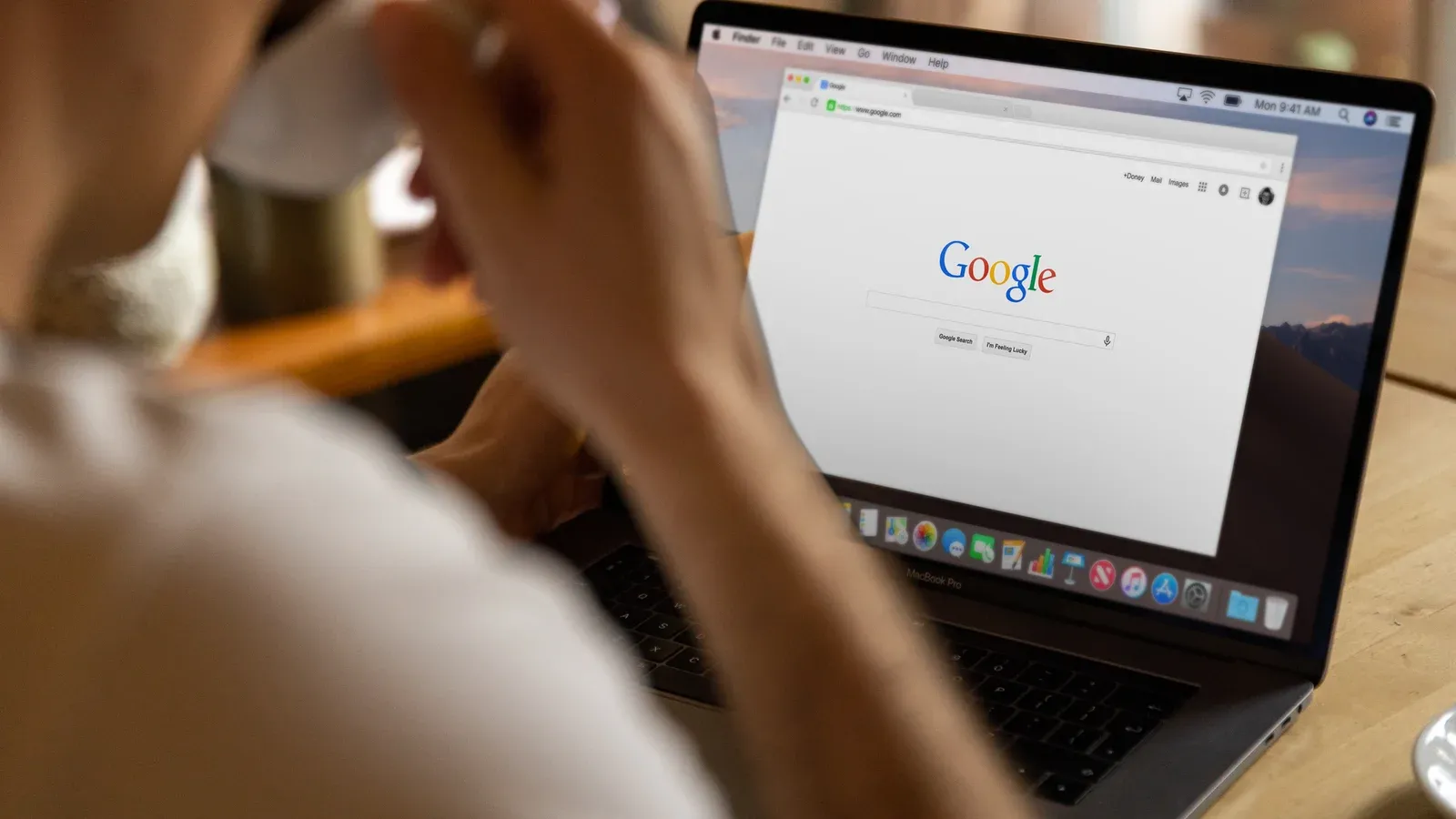 Close-up of an adult drinking coffee and browsing Google on a laptop indoors.