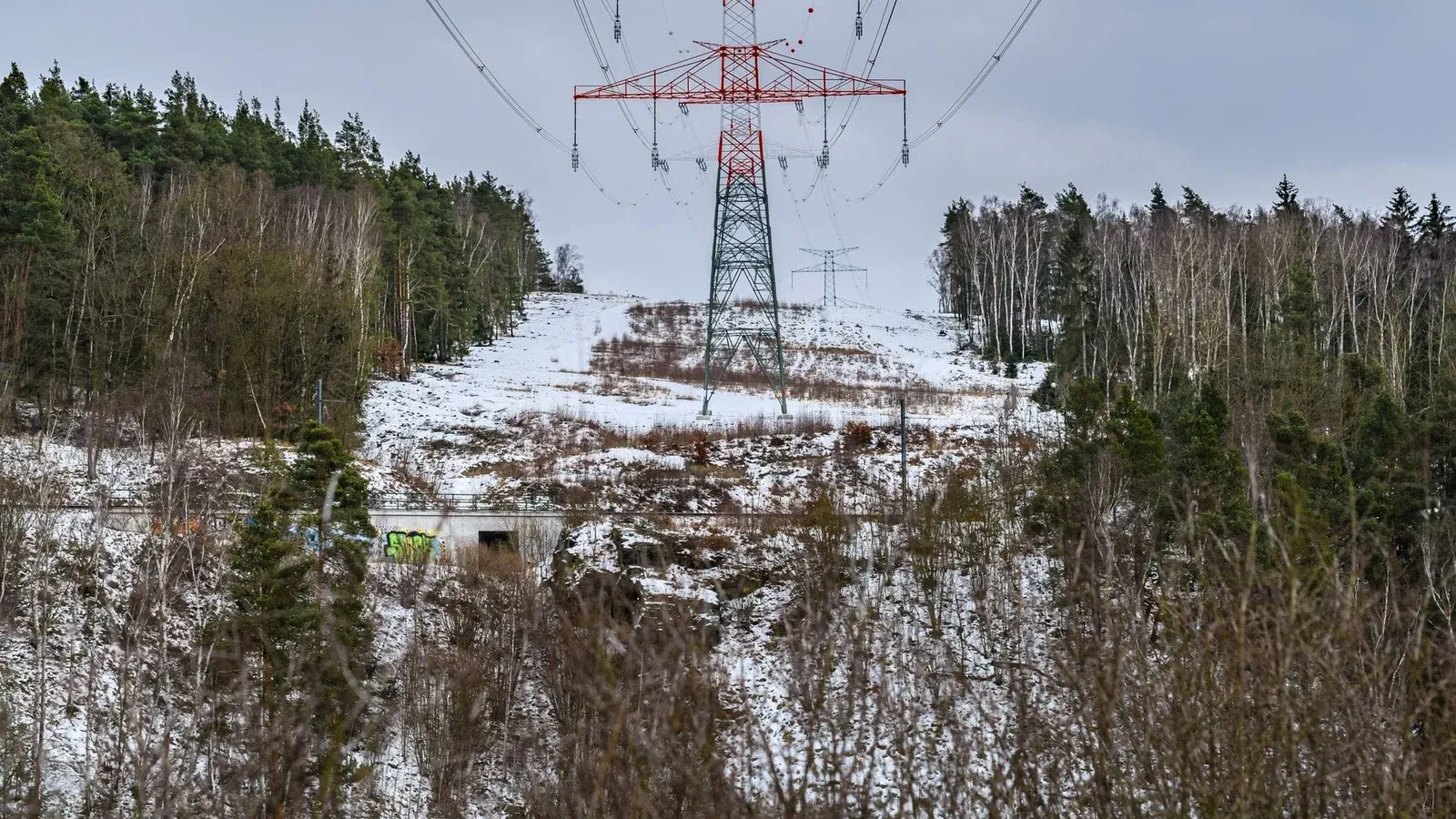 High-voltage power lines stretch through a wintry forest landscape, emphasizing energy and nature.