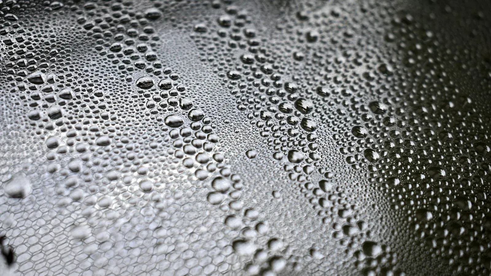 Detailed close-up of water droplets forming patterns on a black surface, showcasing texture and clarity.