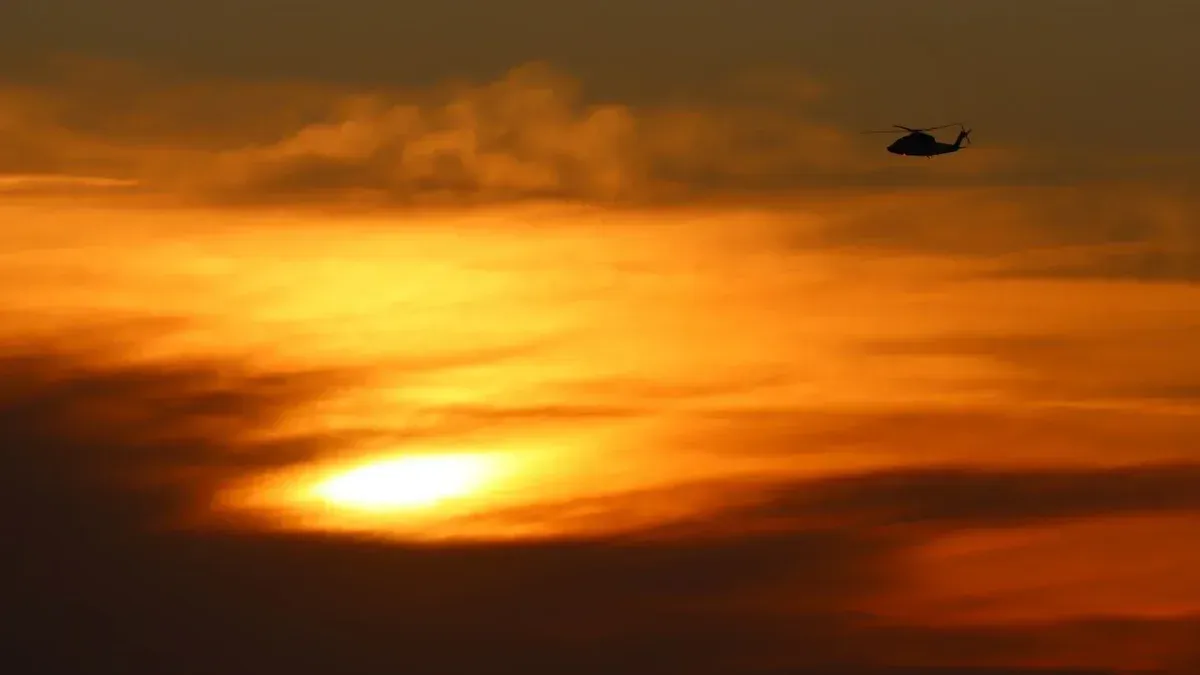 A silhouette of a helicopter flying against a golden sunset sky in Los Angeles.