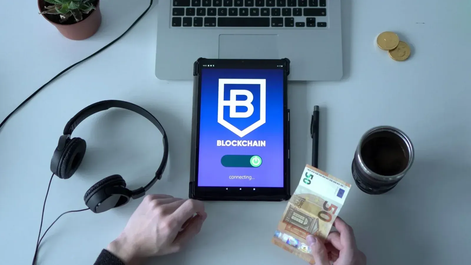 Vista aérea de la tableta digital con la aplicación blockchain, el efectivo y las herramientas tecnológicas en el escritorio.