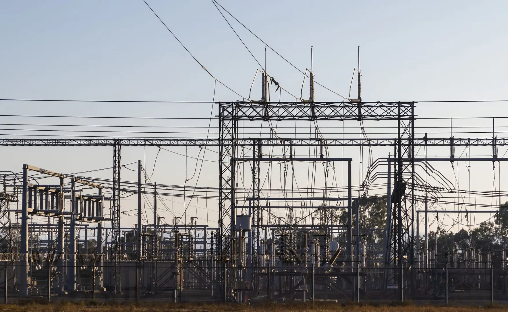High-voltage electrical substation with steel structures and power lines at dawn.
