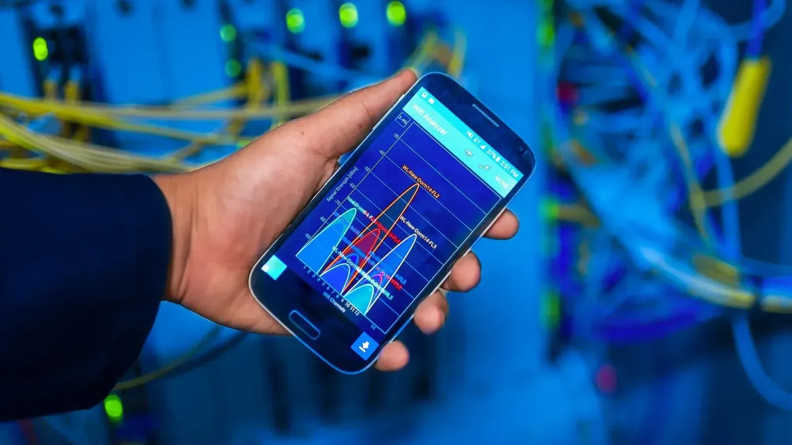 Hand holding smartphone displaying network analysis in high-tech server environment.