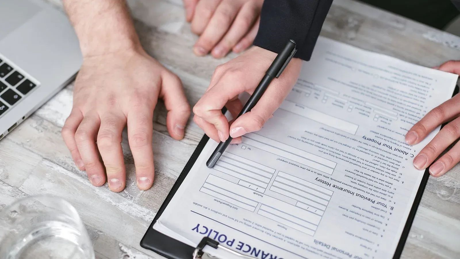 Close-up image of two people signing an insurance policy document on a wooden desk.