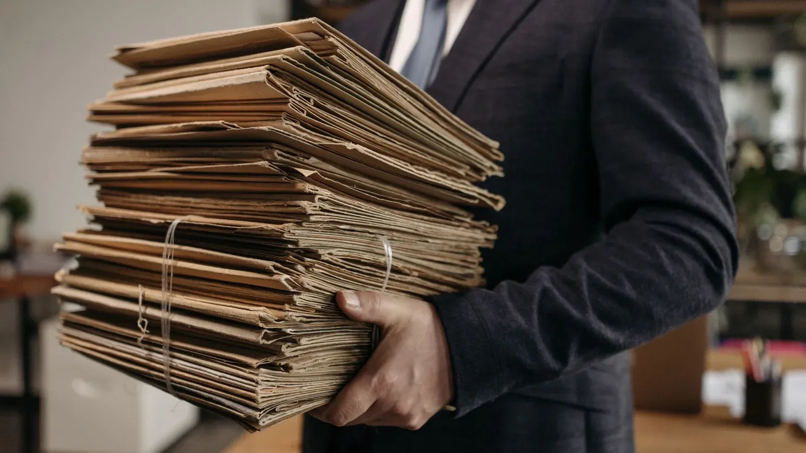 Close-up of business professional holding a large stack of brown folders in an office setting.