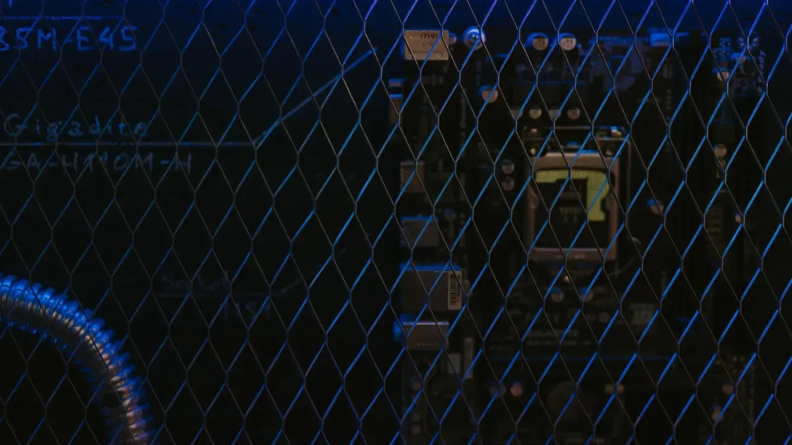 Artistic view of a circuit board through metal mesh with blue lighting.