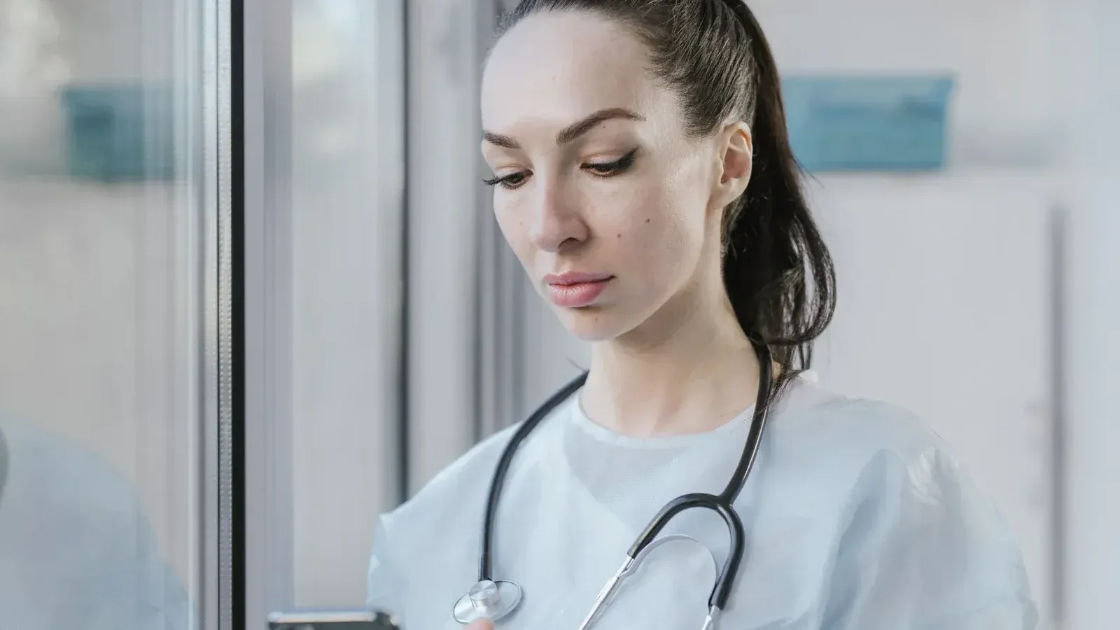 Portrait of a female doctor in a disposable gown using a smartphone in a hospital environment.