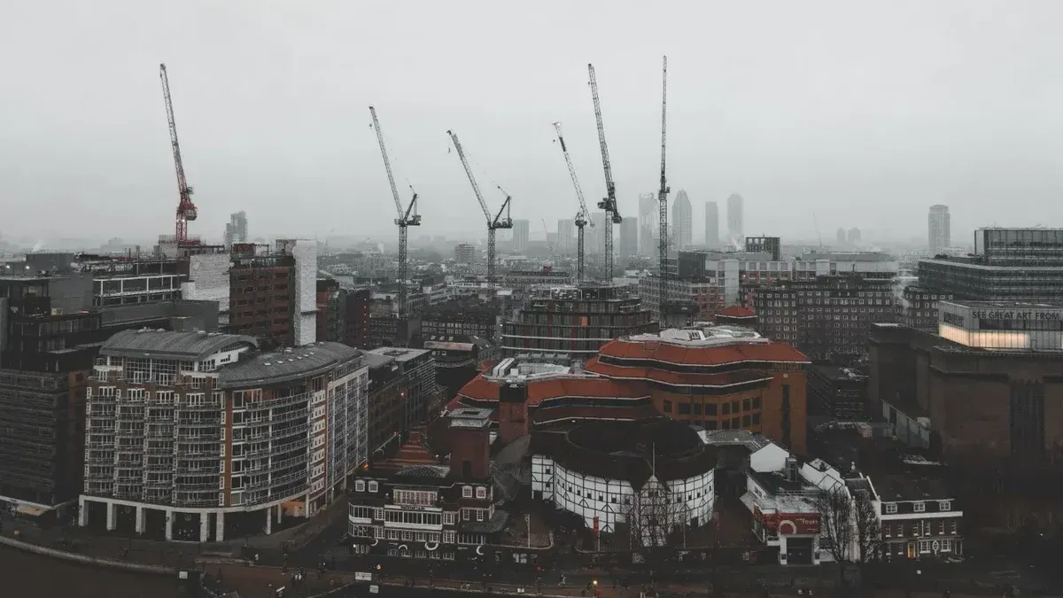 Foggy day in London featuring construction cranes over the cityscape in a moody atmosphere.