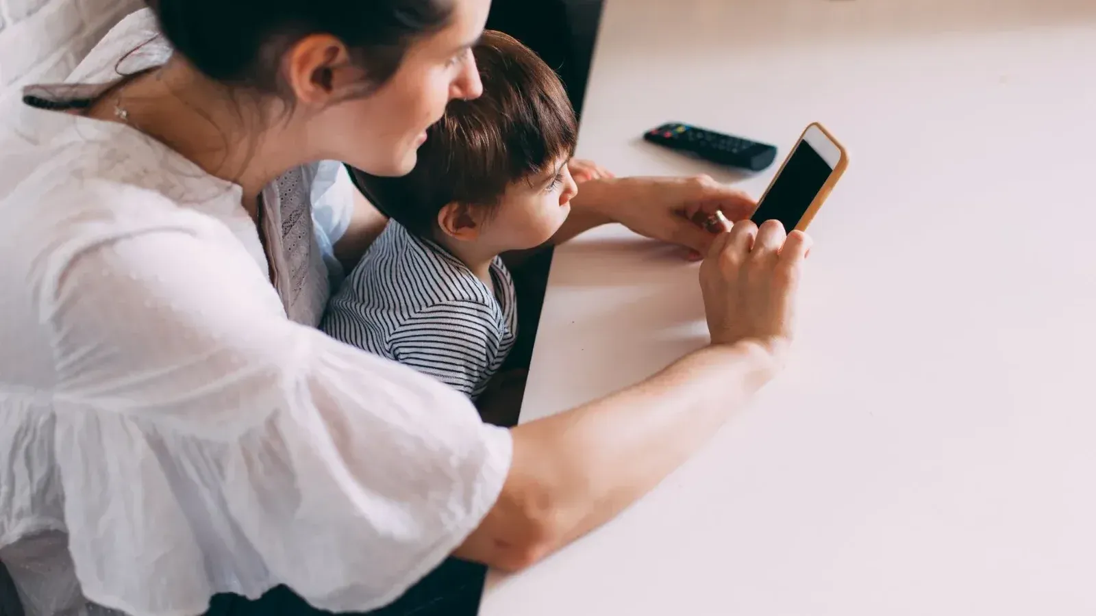 A mother and her child engaging with a smartphone indoors. Perfect for family and technology themes.