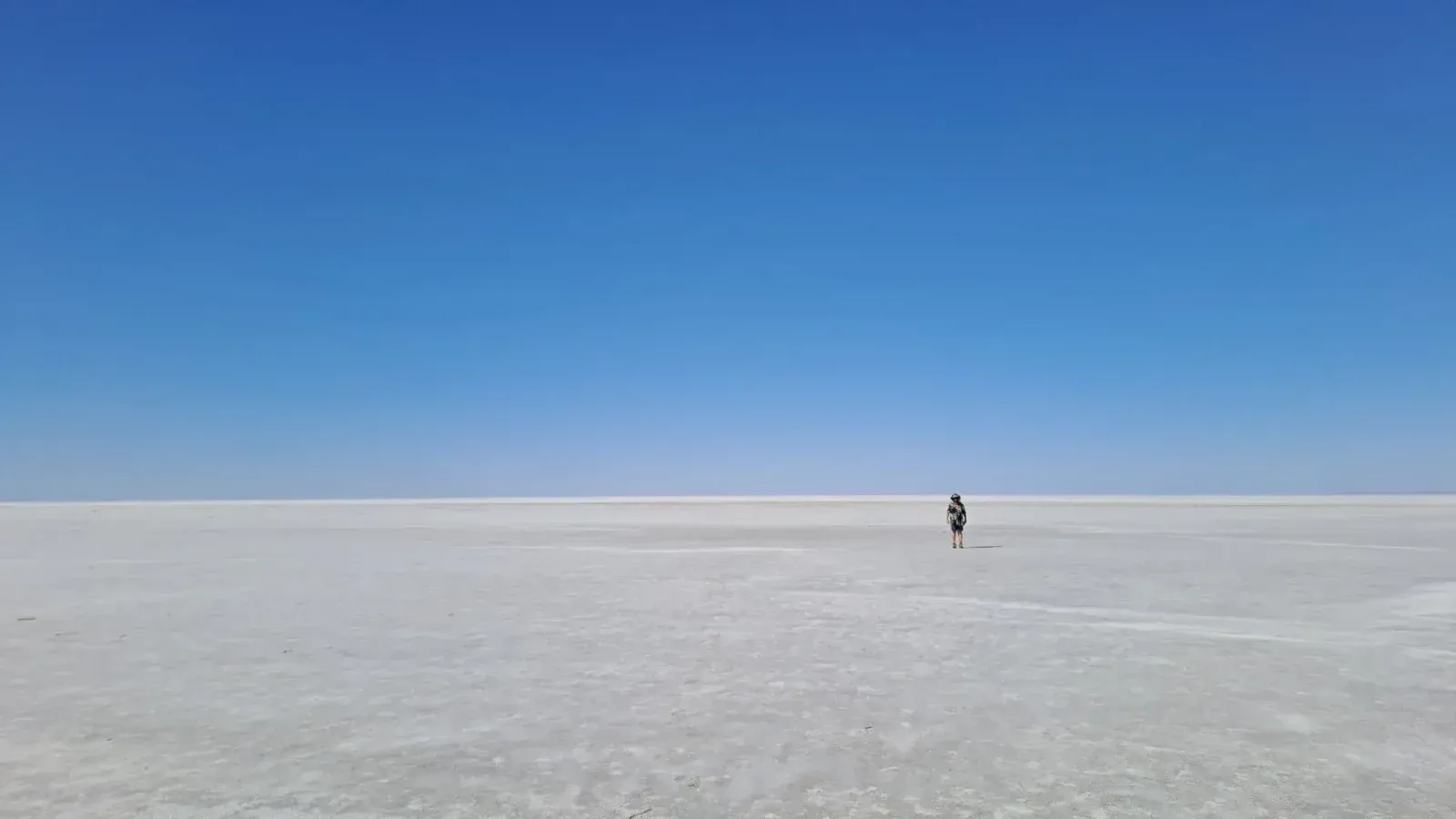 A lone traveler explores the expansive salt flats under a clear blue sky in South Australia.