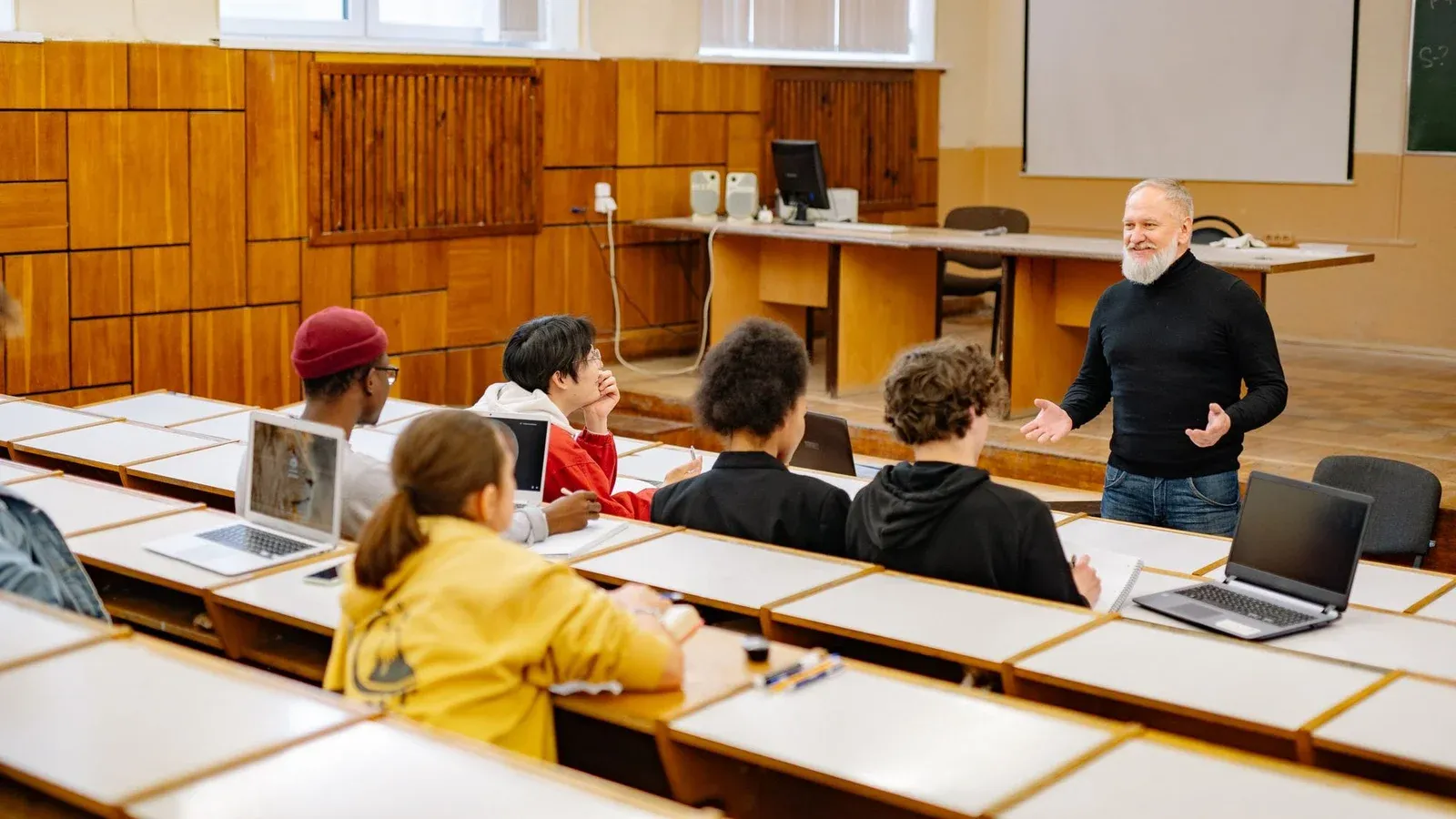 Students engaging with a professor in a university lecture hall, utilizing technology.