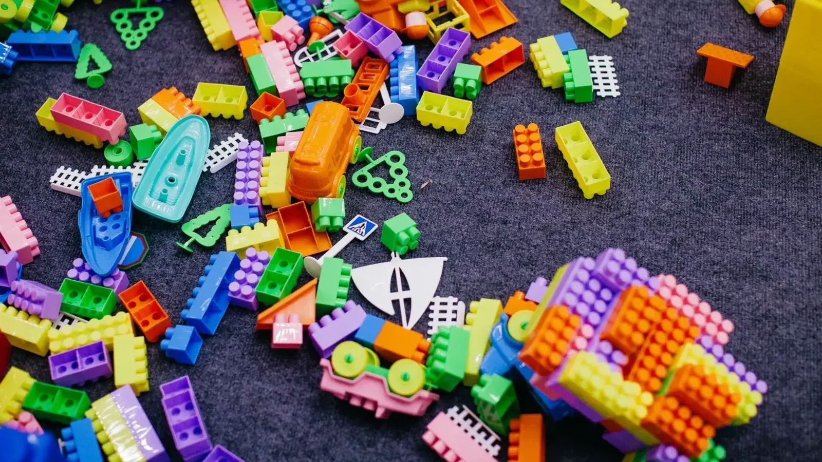 Vibrant plastic toy blocks scattered on a grey carpet, showcasing assorted shapes and colors.