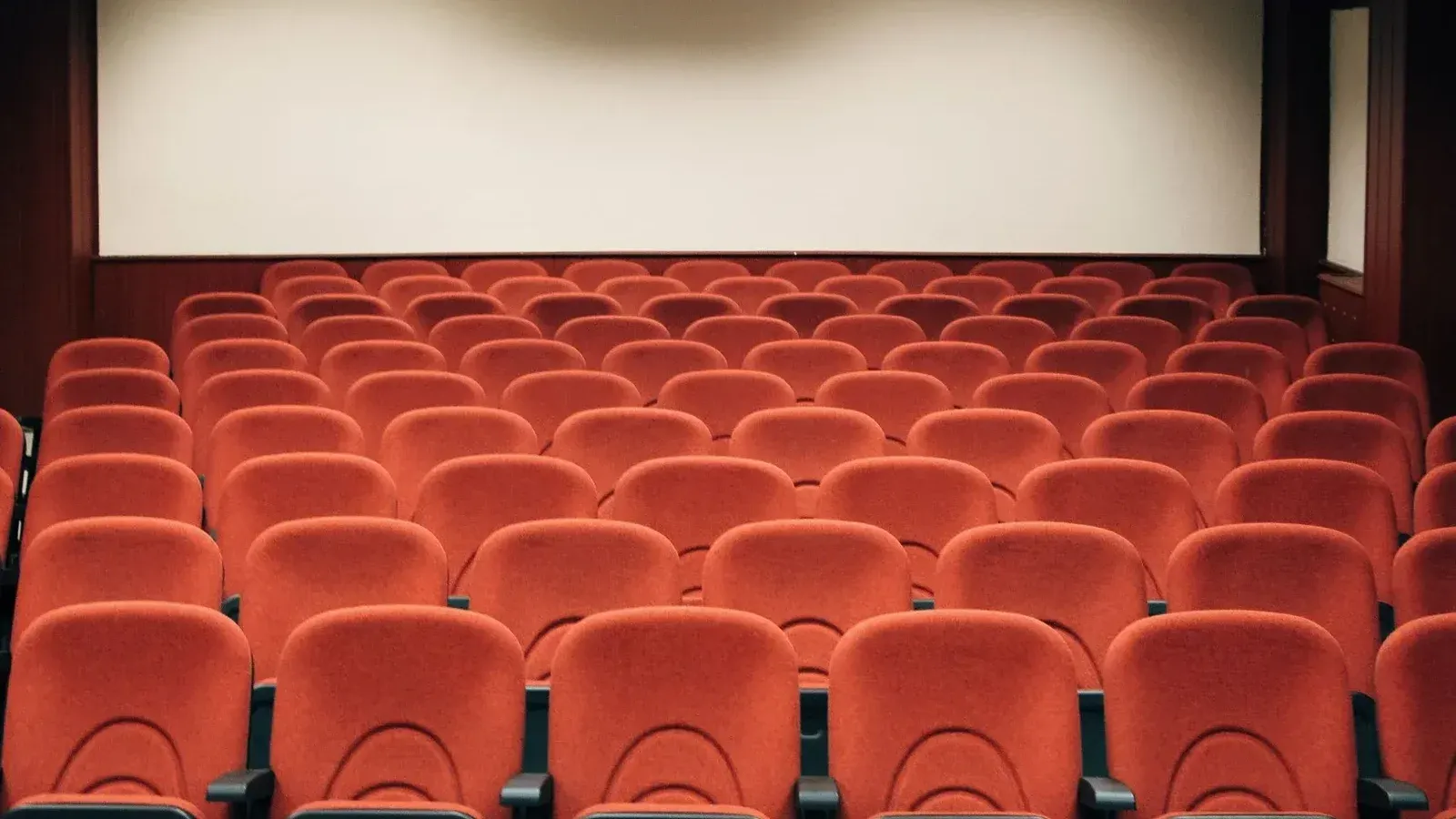 A spacious theater with empty red seats and a large screen, ready for the next audience.