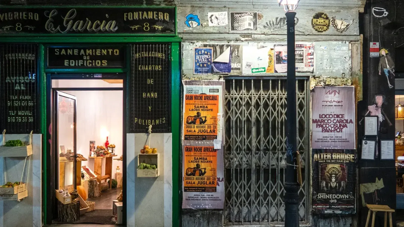 Charming vintage storefront with warm interior lighting and colorful street posters at night.