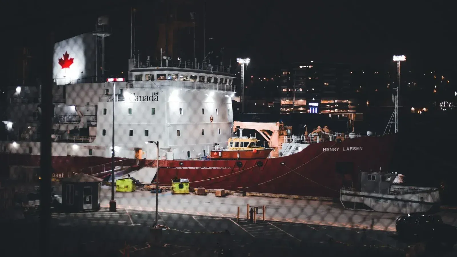 Illuminated Canadian icebreaker ship docked in a harbor at night with city lights in the background.
